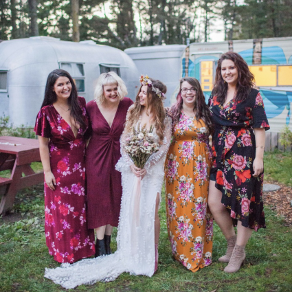 Bride poses with four bridesmaids in colorful dresses in front of vintage trailers